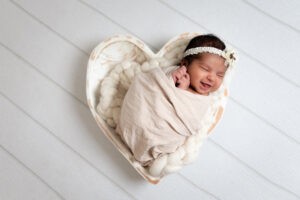 Newborn girl wrapped in heart bowl