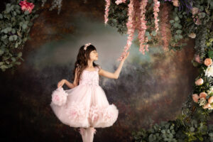 Young Girl under arch of flowers in ballet pose, gently touches pink cascading flowers