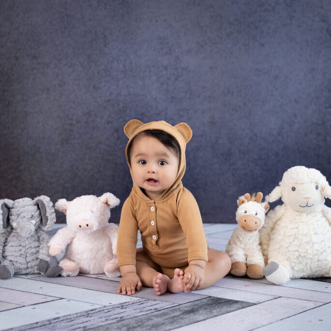 6 month old boy sitting in a line with stuffed animals
